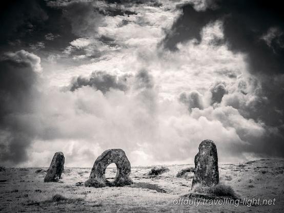 A group of three standing stones, one with a hole through, against a dramatic sky.