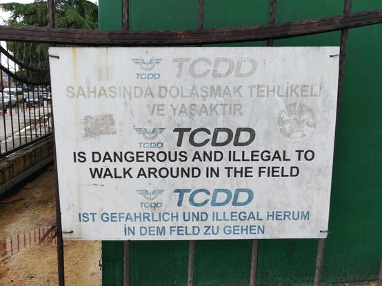 Hinweistafel auf Türkisch, Englisch und Deutsch. Auf deutsch steht der Text "Ist gefährlich und illegal herum in dem Feld zu gehen."