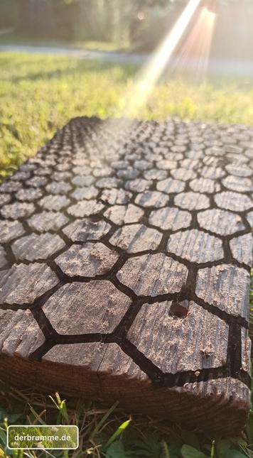 Ein Altholzbrett mit einem Hexagonmuster liegt auf einer Wiese im Abendlicht.