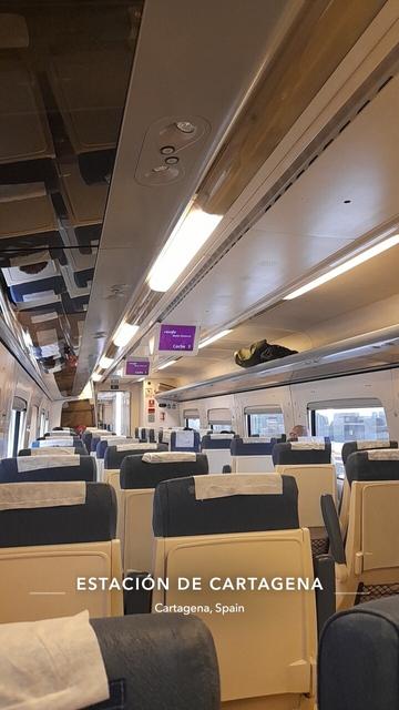 Photograph showing inside the full length of a train carriage with only the top of the sear backs visible with luggage racks text saying estación de Cartagena, Cartagena, Spain
