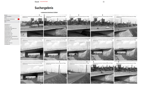Screenshot des Kasseler Stadtarchivs nach "unbekannter Aufnahmeort" + "1957" zeigt eine Brücke unter der eine Dampflokomotive verkehrt mit einer Industrieanlage im Hintergrund.