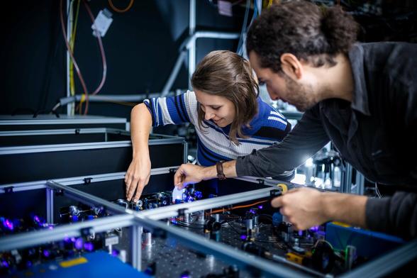 Woman happily adjusting an optical element on an optical bench with a blue laser. A man assists by holding a piece of paper into the beam.
(C) Jan Hosan