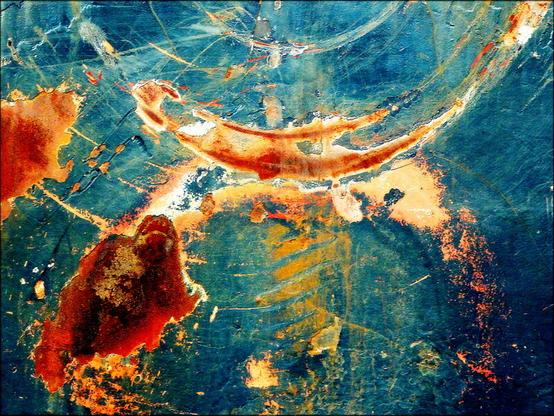 A colour photograph showing patches of rust and arcing scratches on a black painted boat hull.  Large concentric arcs of rust flow through the top of the frame with large patches of rust below rather resembling a cosmic scene.