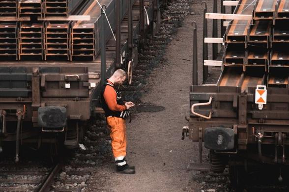 Worker leaning on a train cart, looking at his phone