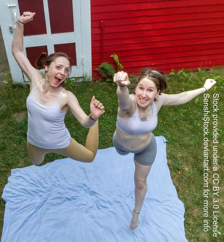 Two people leaping into the air. One is holding her hands up and her legs are coming up behind her. The other is pointing a fist towards the camera and has one leg extended.