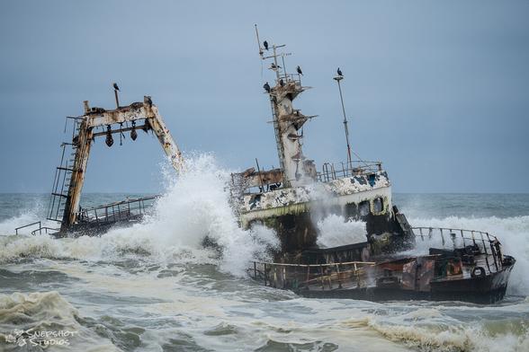 Shipwreck with waves crashing through openings in the hull and deck