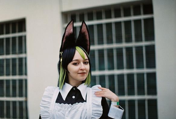 A head-and-shoulders portrait of a cosplayer girl wearing maid outfit and kemonomimi (wolf ears probably) turning her head to her left and looking to the camera