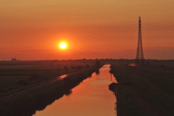 Setting summer solstice sun almostaligned with Haddiscoe cut turning the water and nearby railway tracks golden, outsized pylons taking the national grid high above the water to safely clear large sailing vessels of the kind you don't get much anymore, all orange and yellow with some detail in the fields