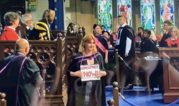 Student at graduation cermony with placard around their neck reading "renegotiate now."