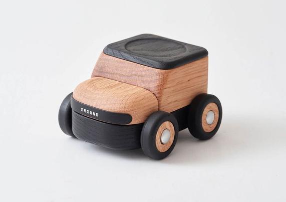 A minimalist toy car made out of wood by Korean studio S2 VICTOR in natural and dark wood tones, with soft rounded edges.