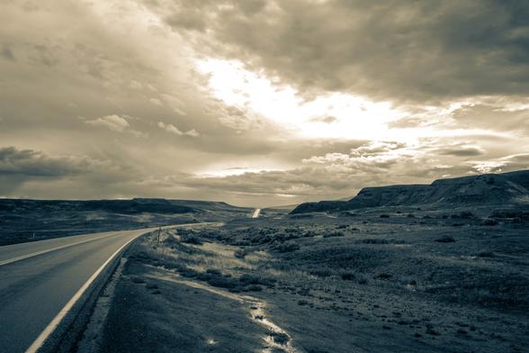 A split tone monochromatic photo of a ribbon of rain slicked highway cutting through the dobies between Hotchkiss and Delta, Colorado, USA