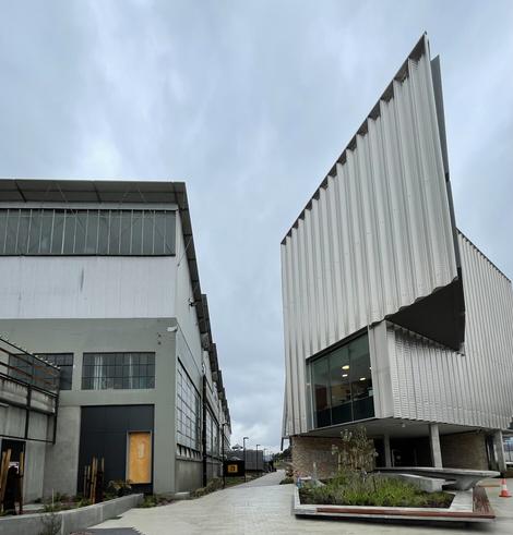 A laneway runs between two buildings. The one on the left is an old rolling stock workshop. Its basically a rectangular shed. The one on the right is brand new and architecturally designed energy efficient building with all sorts of angles and peaks. Lots of big windows and shades.