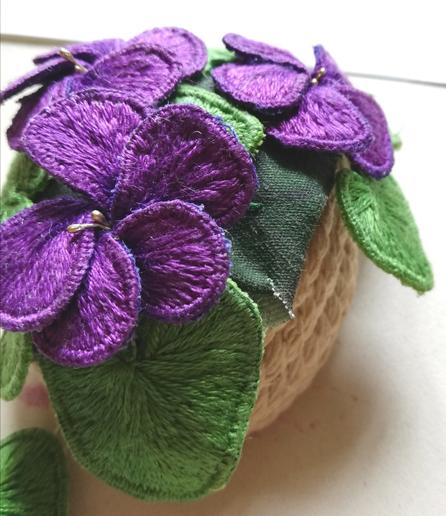 Close-up of some violets in stumpwork being attached to the coiled cord pot. Some of the base fabric is showing, which it shouldn't be!