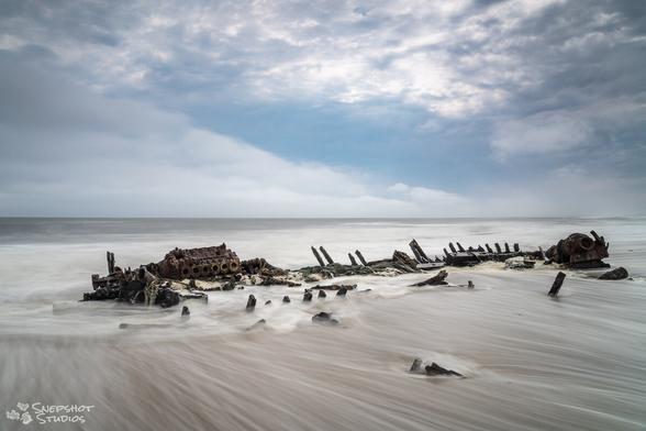 Sparse remains of a ship on the beach with the water flowing out, leaving streak patterns.