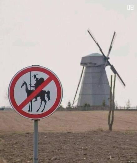 Photo of a windmill in the background, in farmers fields, with a not allowed sign (red circle with slash) over a silhouette of don quixoti