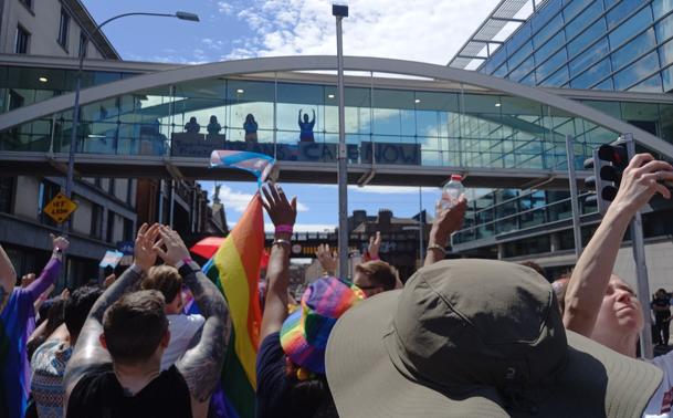 Dublin Pride Parade in Pearse Street people waving flags from to street and over on the bridge people with support signs cheering