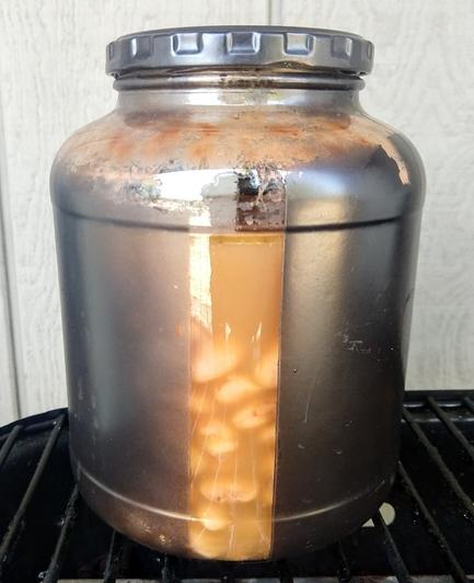 A glass pickle jar painted black except for a clear vertical strip, cooked beans visible inside.