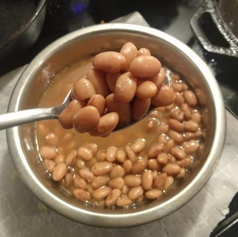 Cooked pinto beans in broth in a bowl with a spoon.
