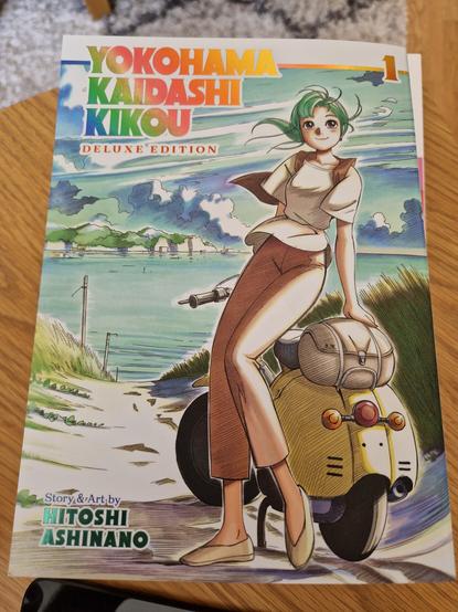 The cover of the first volume of Yokohama Kaidashi Kikou in the deluxe edition from Seven Seas. Story & Art by Hitoshi Ashinano.

Alpha is standing by her scooter, facing us with a smile, an inundated landscape in the background.