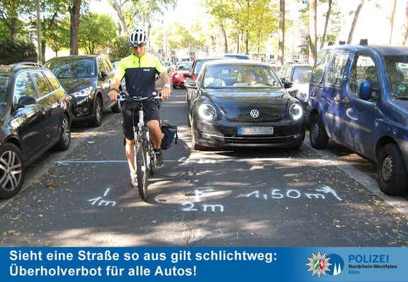 Infografik der Polizei NRW.
Eine ~4m breite Straße, links und rechts parken Autos, eine Person auf einem Rad fährt leicht zur linken Seite ein Auto dahinter versucht zu überholen.
Auf dem boden sind von der linken seite an die sicherheitsabstände und breite des fahrrads markiert.
1m abstand von parkenden autos, 1m breite des fahrrads, 1,5m sicherheitsabstand.
Es bleiben noch ~50cm übrig.
darunter der Text "Sieht eine Straße so aus gilt schlichtweg: Überholverbot für alle Autos!"