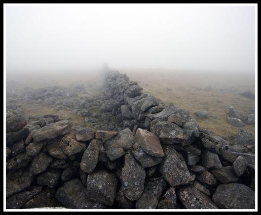 Picture of a stone wall on the top of a hill covered with low cloud.