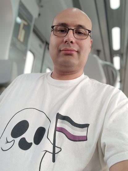 Selfie en un cercanías
Yo con una camiseta blanca con un fantasmita que lleva una bandera asexual.