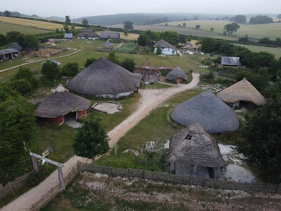 A replica of an iron age enclosure with thatched circular buildings at Butser Ancient Farm museum.