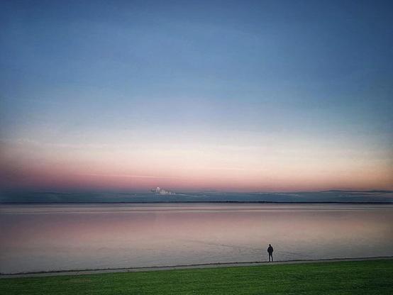 A man standing on the banks of Wilhelmshaven's South Beach, looking into a sunset.