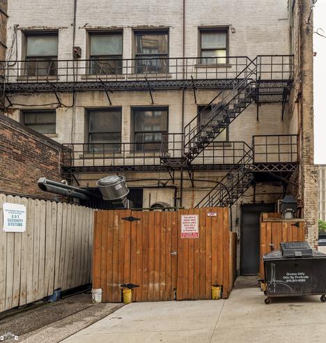 E.9th. Place
-June 27, 2023
 .
The backside of this Huron building is littered with warning signs and cheap security cameras to the point of ridiculousness.
At first I was puzzled by all the odd buckets and pails under that fence until I realized that they’re being used as mooring for the posts.