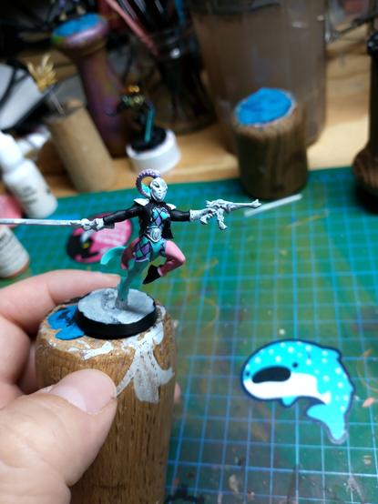 A partially painted eldar harlequin miniature. Green and purple checks are visible on the shirt and pants