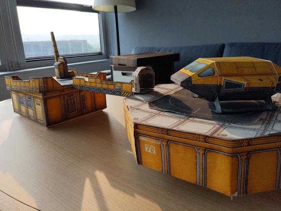 Paper scenery on hotel table. Yellow sci-fi rooftop and helipad connected by a walkway.

Yellow shuttlecraft on pad.