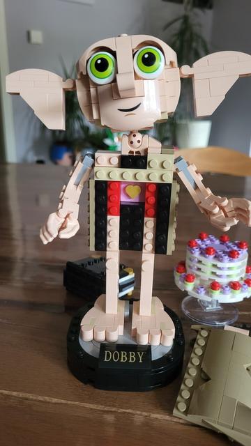 Dobby der Hauself von Lego mit geöffneter Toga, die sein goldenes Herz im Inneren zeigt. Im Hintergrund liegt das
 Tagebuch von Tom Riddle und die schwebende Torte.