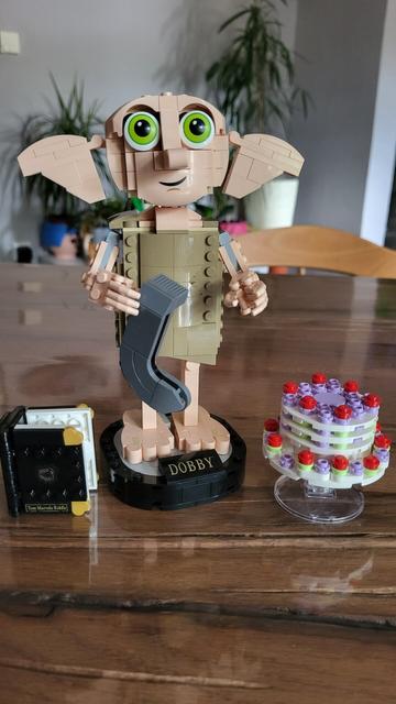 Dobby der Elf, gebaut aus Lego, steht auf einer Basis mit seinem Namen. Er hat eine Socke in der Hand. Neben ihm steht die schwebende Torte und das Tagebuch von Tom Riddle.