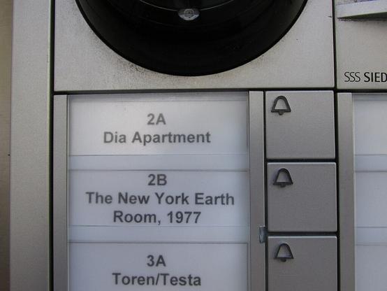 WikiCommons color photo shows a detail of a modern metal wall panel of 3 apartment/flat doorbell buttons. The top one is labeled "2A Dia Apartment", the second one is labeled "2B The New York Earth Room" and the next one says "3A Toren/Testa". A visitor to the New York Earth Room presses the second button to be let upstairs.  

Caption: " Buzzer for the New York Earth Room by Walter De Maria" 
Photo by Found5dollar, 2020.

https://commons.wikimedia.org/wiki/File:New_York_Earth_Room_1.jpg