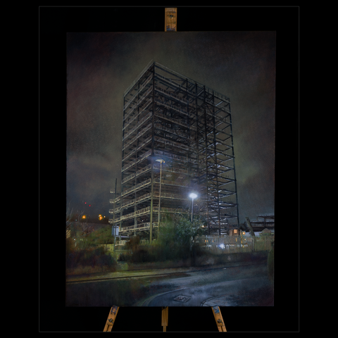 What can be seen is the scaffolding supporting the making of a tower for a new residential block. The scene is at night. A dark brooding cloudy sky fills the space behind the tower. Two bright street lights sit in front of the tower, giving some of the metal beams, struts, and supports a glow of light. Other parts are left in dark silhouette. The tower has a strong skeletal feel, ominous, eerie and threatening.