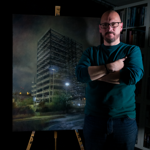 Andy stands on the right side of the image next to the painting in his darkened studio