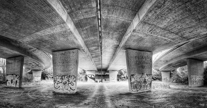 A b/w wide-angle view underneath a concrete motorway bridge.