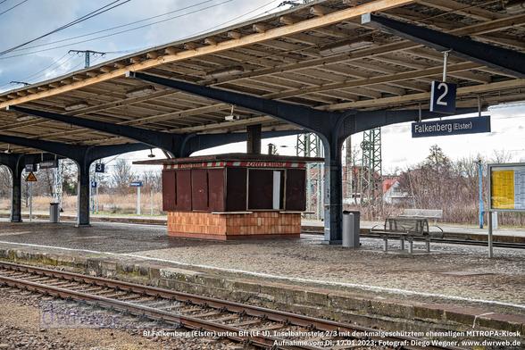 Der ehemalige MITROPA-Kiosk auf dem Inselbahnsteig 2/3 steht unter Denkmalschutz. Nach der Wende 1989/90 wurde er, der Bandenwerbung zufolge, offenbar als "Ottis Kiosk" weiter betrieben. Am 17.01.2023, als dieses Bild entstand, konnte man weder hier noch sonstwo im oder am Bahnhof Falkenberg (Elster) Verpflegung kaufen. Laut der Plangenehmigung des EBA vom 05.09.2022 zum Umbau der Verkehrsstation des unteren Bahnhofsteils muss dieser Kiosk erhalten bleiben. Es ist typisch für solche Verkaufseinrichtungen, wie sie die MITROPA bis 1990 auf vielen (auch kleineren) Bahnhöfen in der DDR betrieb. Im Vordergrund verläuft das Gleis 2M (= Kundengleis 2), auf der anderen Bahnsteigseite das Gleis 5M (= Kundengleis 3).