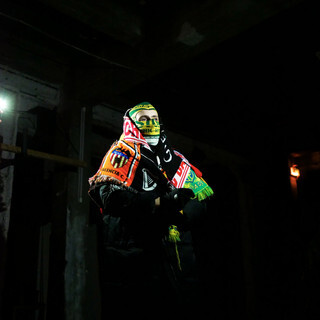 Coco Fran6 sur scène avec sa cagoule et ses écharpes de supporter.