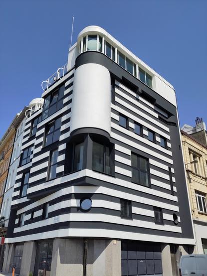 Corner building at boulevard Antwerpen. Facade with black and white stripes, Memphis-style architecture with cubes, columns and round windows.