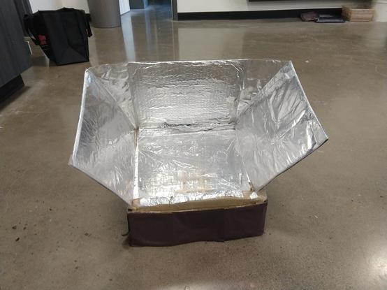 Picture of homemade solar cooker with slanted top, in indoor setting on concrete floor