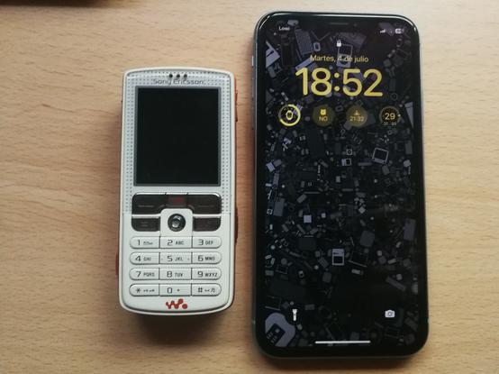 Comparación de tamaño de un Sony Ericsson W800 blanco con el marco naranja. La pantalla es pequeña y tiene botones de colgar, descolgar, retroceso y cancelar. También un jostick para moverse por los menús. Ya debajo de todo eso el teclado numérico. El iPhone es enorme comparado con este y es sólo pantalla.