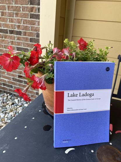 Cheerful photo of “Lake Ladoga: The Coastal History of the Greatest Lake in Europe,” posed outdoors next to a pot of flowers.