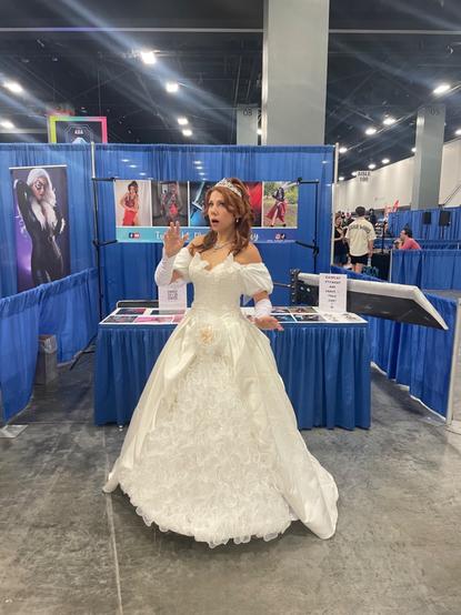 A woman cosplays as Giselle from the Disney movie Enchanted. She wears a large fluffy wedding dress and looks surprised.