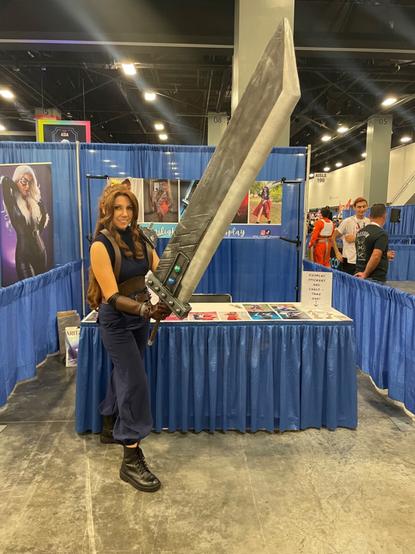 A woman is cosplaying Aerith from Final Fantasy 7. She wears the uniform of Cloud Strife and holds the buster sword.