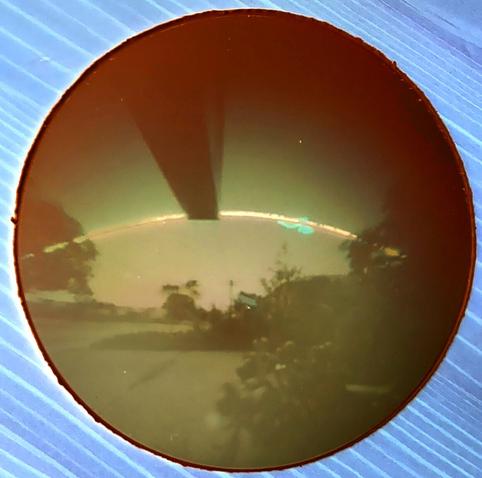 A view down a suburban street, with a sign directly overhead and in line with the view. The arc of the sun's path is across the middle of the image, which is in shades of brown and orange.
