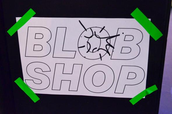 White A4 sign sticked on a black surface, mounted with green tape, saying: BLOB SHOP (with a sweet exploding "O" illustration on top)