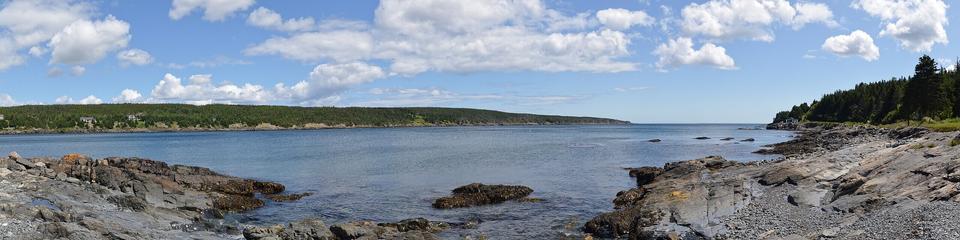 A panoramic photo of a long bay under a sunny sky with white clouds.