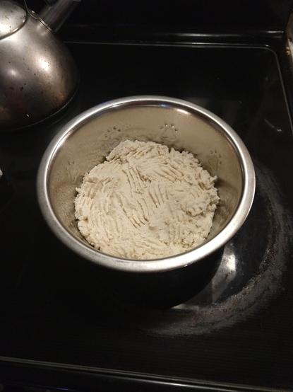 What the shortbread looked like before baking, white dough in a stainless steel round pan with marks from pressing down with a fork