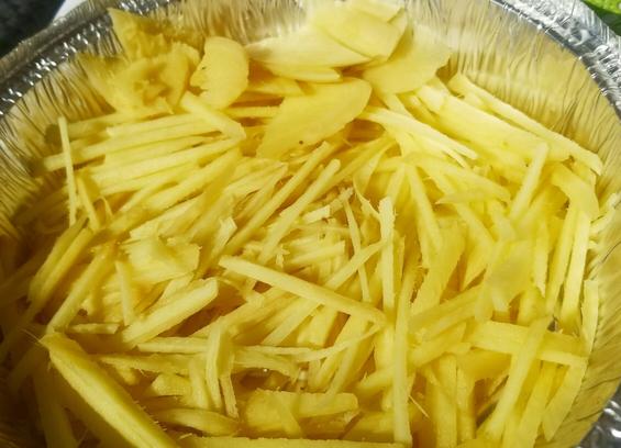Sliced ginger being fermented in preserved mung bean juice, in the sun, in aluminum take out container.